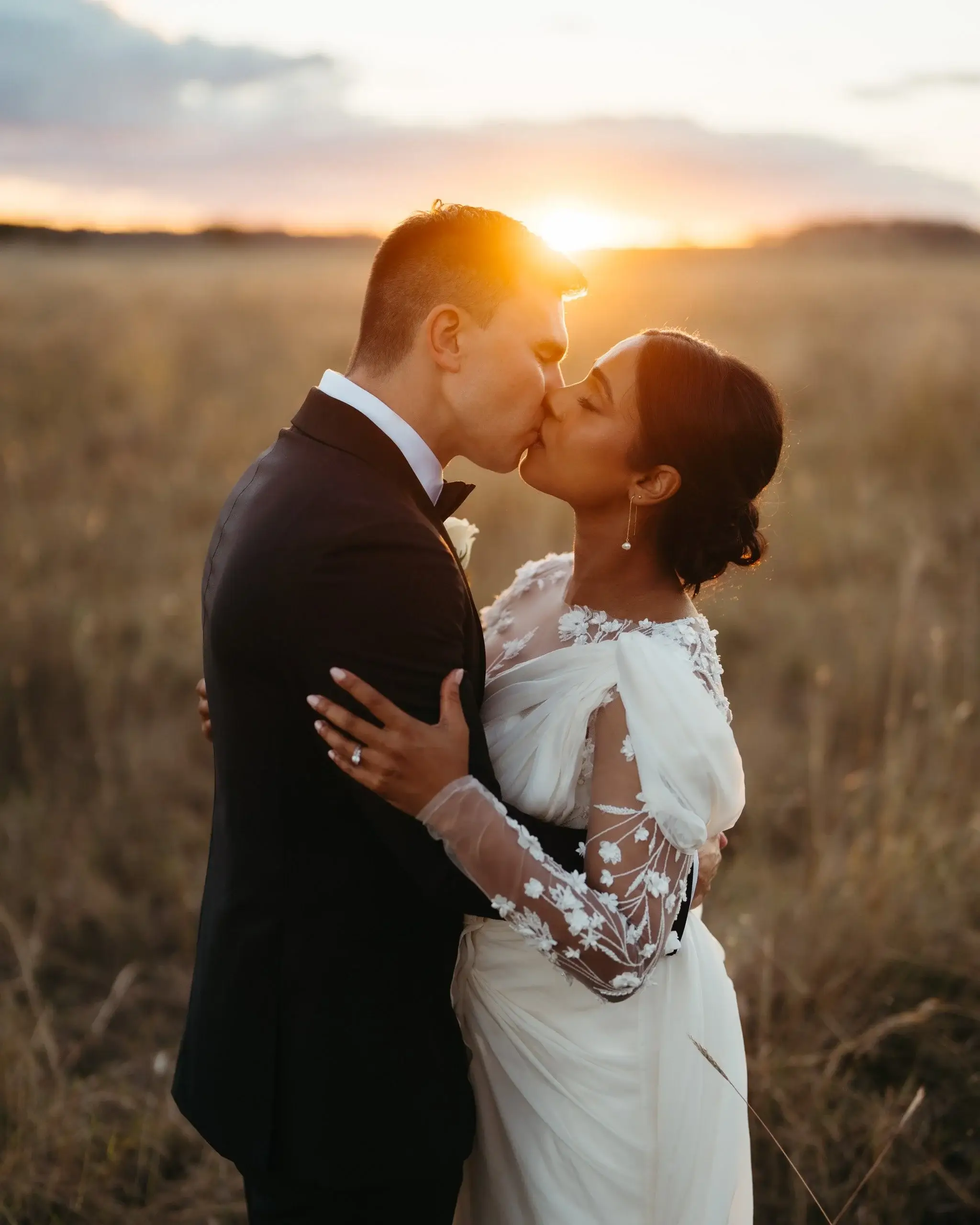 A couple kissing in a golden field at sunset, the sun flaring behind them