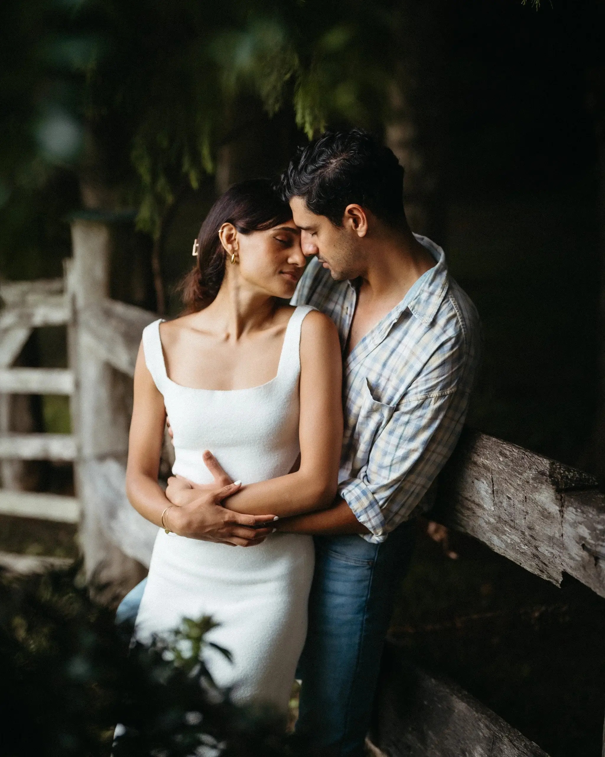 A couple standing close in front of a garden fence at dusk