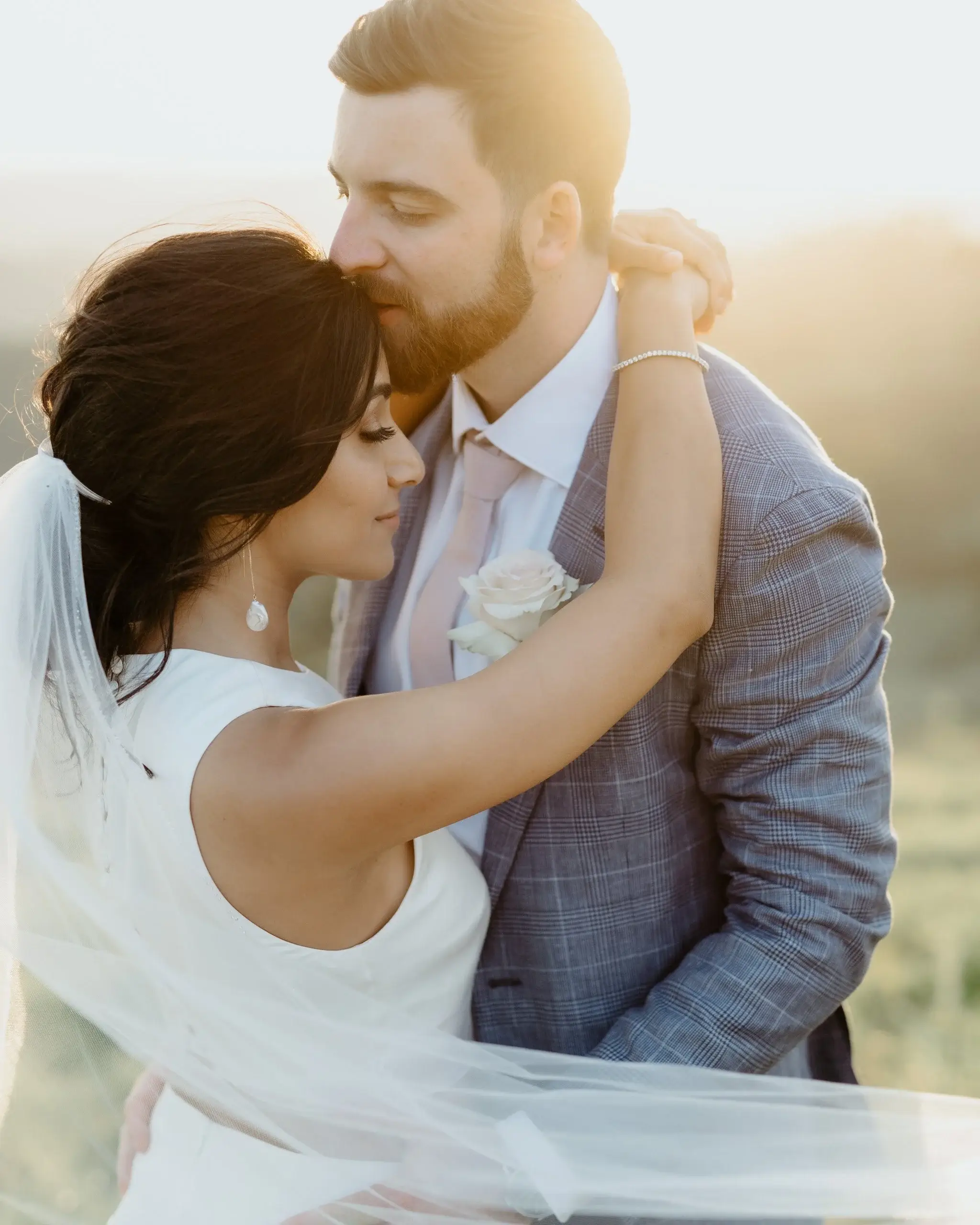 A couple kissing in warm backlight, the bride’s veil catching the sun