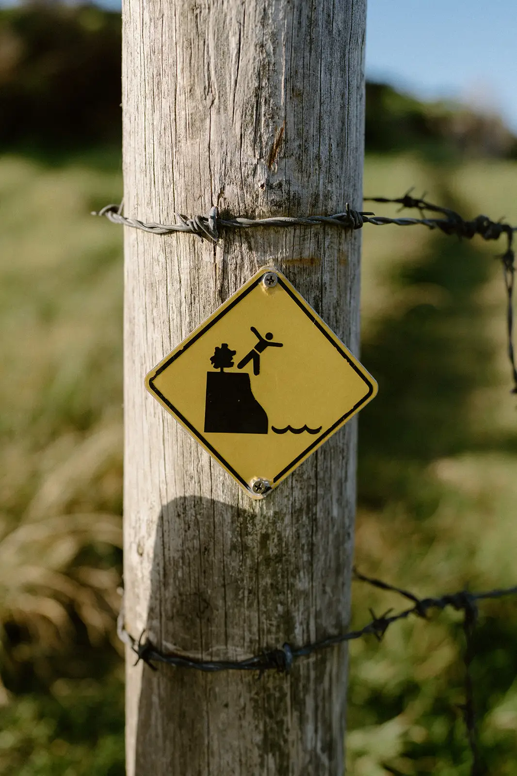 A cliff hazard warning sign on a barbed-wire fence post, Lord Howe Island