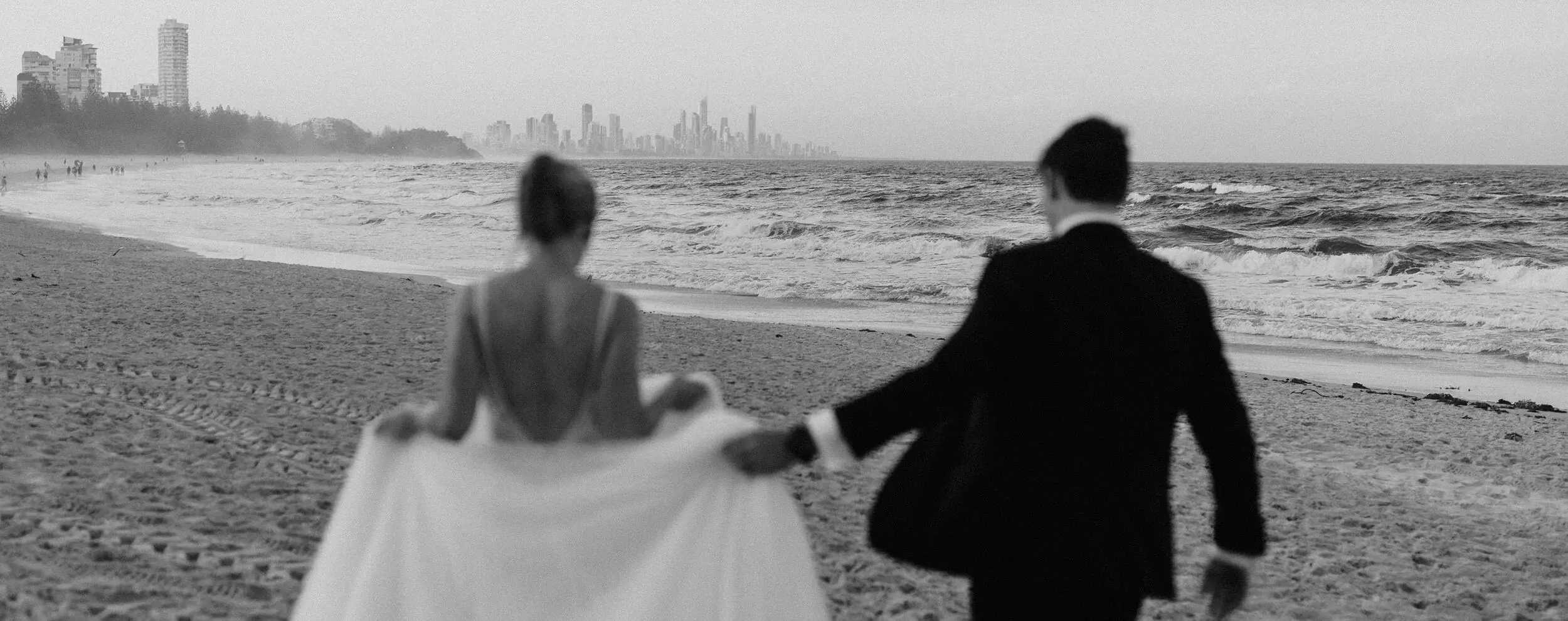 Clair and James on the sand at Burleigh Heads, the headland behind them